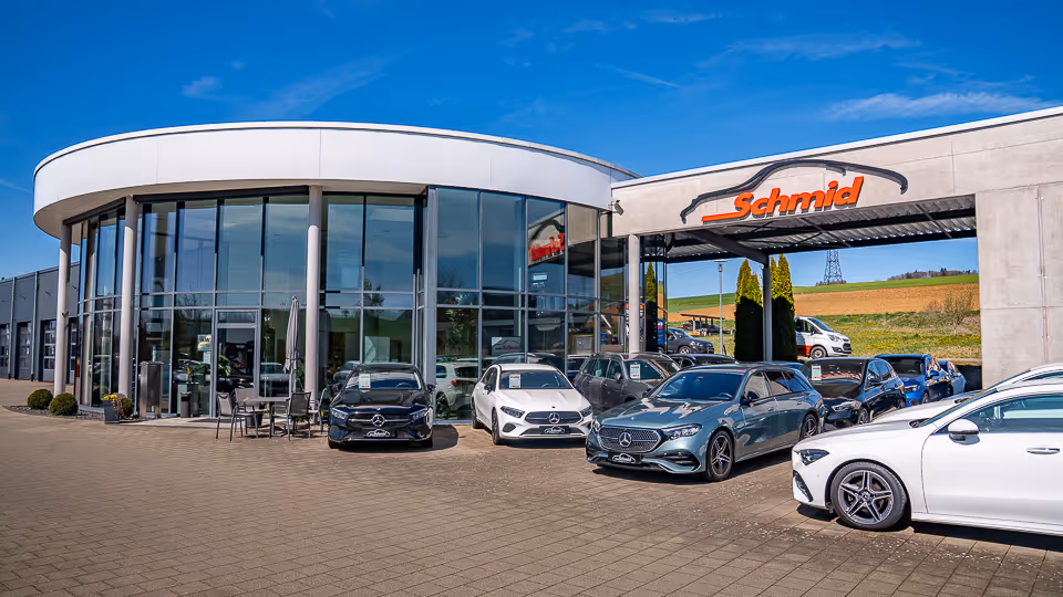 Außenansicht: das Autohaus Schmid mit rundem Glasbau und Mercedes-Fahrzeugen auf dem Vorplatz