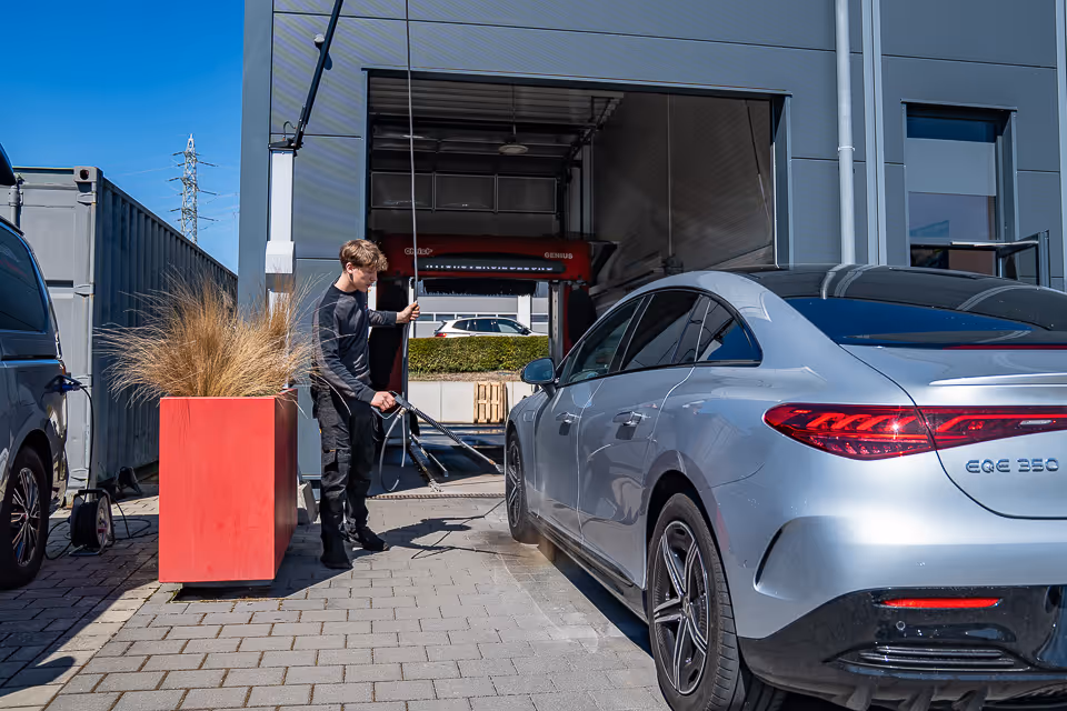 Mitarbeiter wäscht einen silbernen Mercedes mit der Waschlanze vor der Einfahrt der Waschhalle