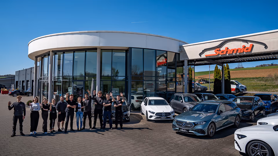 Gruppenfoto des Teams vor dem verglasten Ausstellungsgebäude des Autohauses Schmid in Tengen, im Vordergrund parkende Fahrzeuge